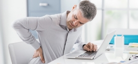 Man sitting at computer with hand on lower back